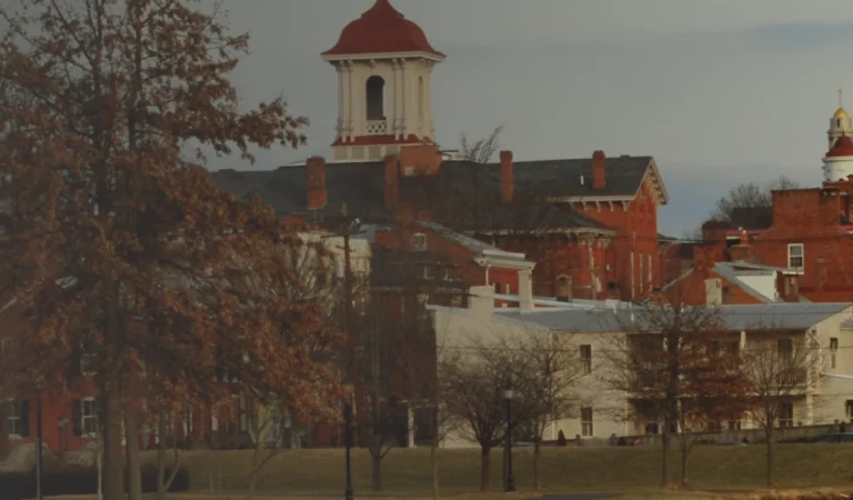 Panoramic view of a small town with historic red brick buildings, white steeples, and a bridge in the foreground.