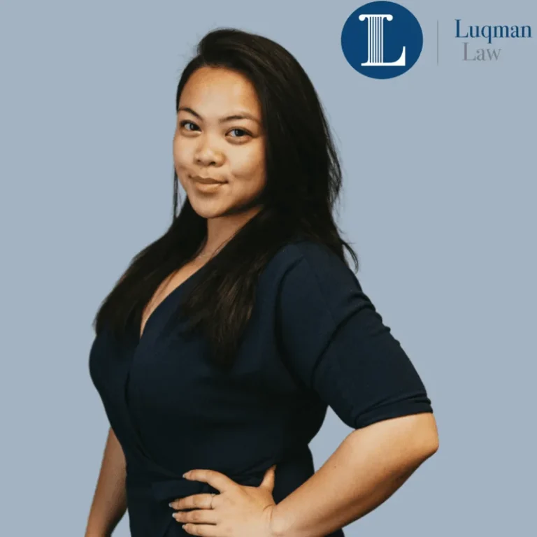 Confident Asian woman in dark blue dress standing with one hand on hip against a light blue background, next to the Luqman Law logo.