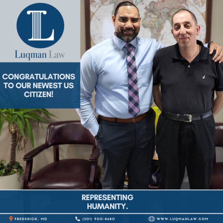 Two men standing in an office, with the man on the left in a light blue shirt and striped tie smiling next to another man in a black polo shirt. A logo of Luqman Law and text congratulating the newest US citizen are displayed, with a backdrop of a world map and a leather chair.