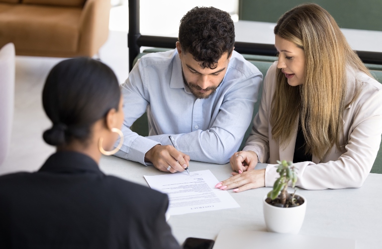 married couple signing document with lawyer