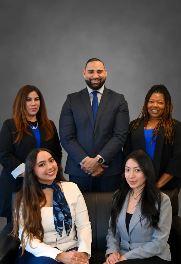 Professional group portrait of five diverse businesspeople in formal attire against a gray background.