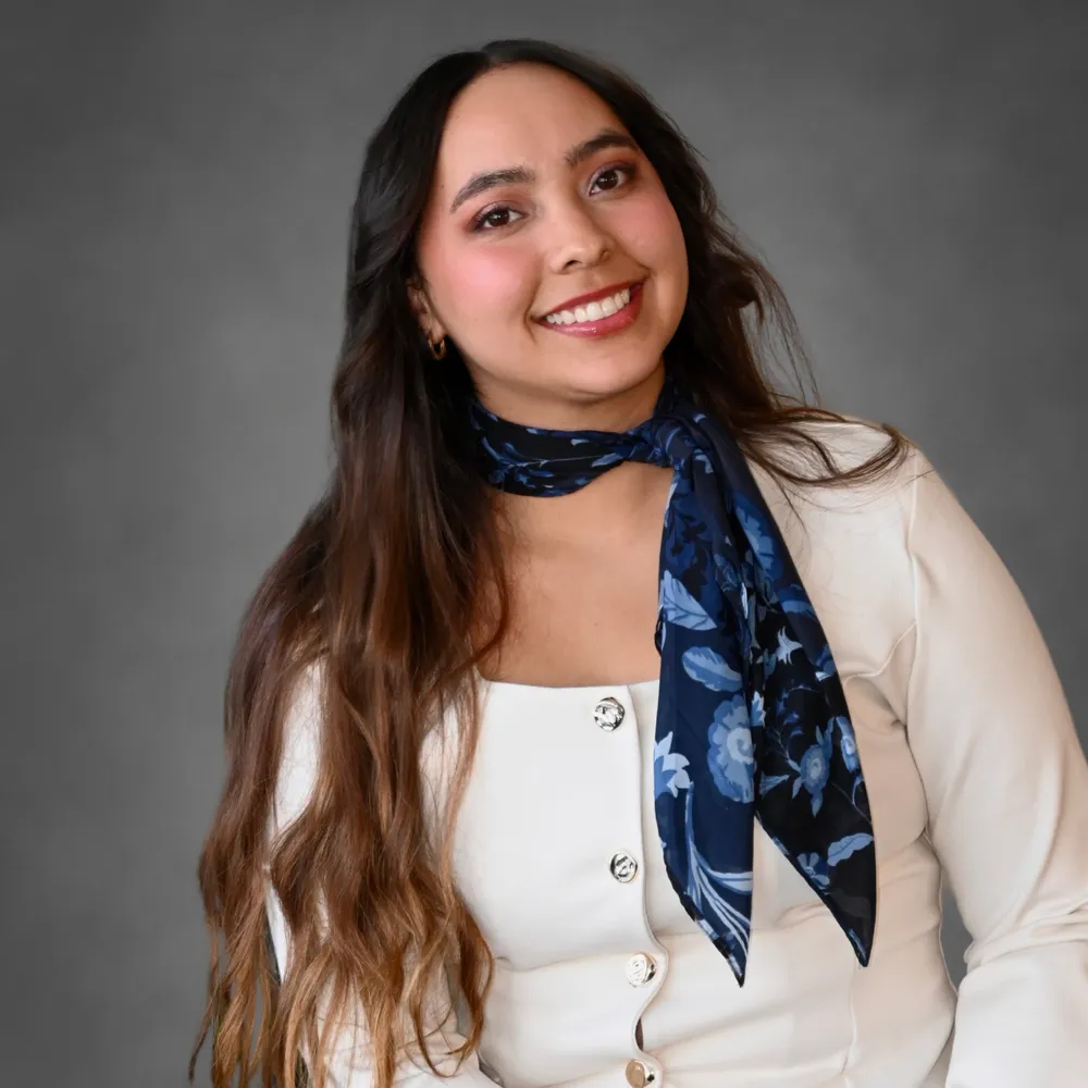Portrait of a smiling woman with long brown hair, wearing a white buttoned top and blue floral scarf.