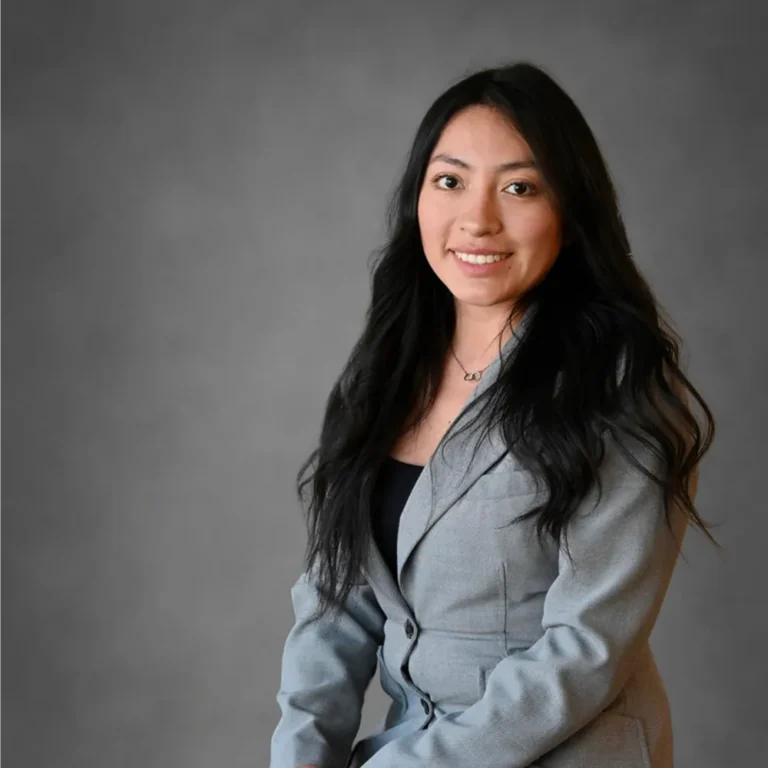 Professional portrait of a smiling woman with long black hair wearing a gray blazer.